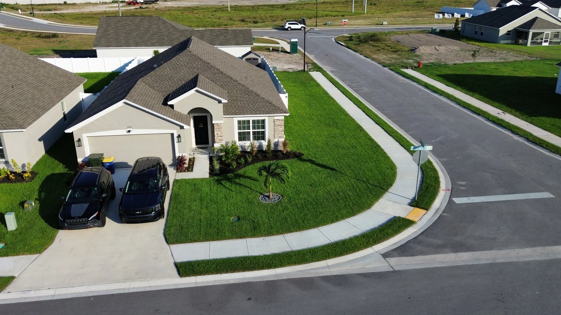 Aerial view of a modern family home featuring a manicured lawn, two parked cars, and a welcoming entrance in a suburban neighborhood